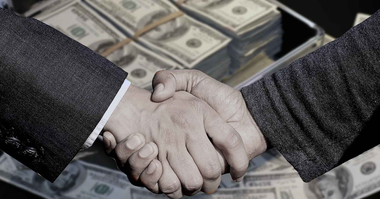 two men shaking hands over backdrop of cash