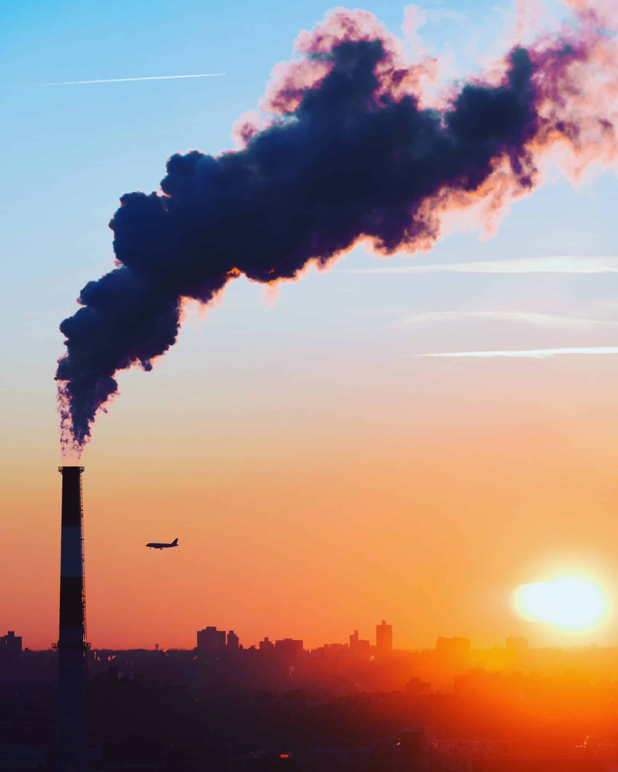 Silhouette of smokestack in front of orange NYC sunset with an airplane in the foreground.