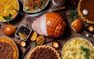 A traditional thanksgiving feast with pies, mashed potatoes, dressing/stuffing, gravy, and a large turkey in the middle.