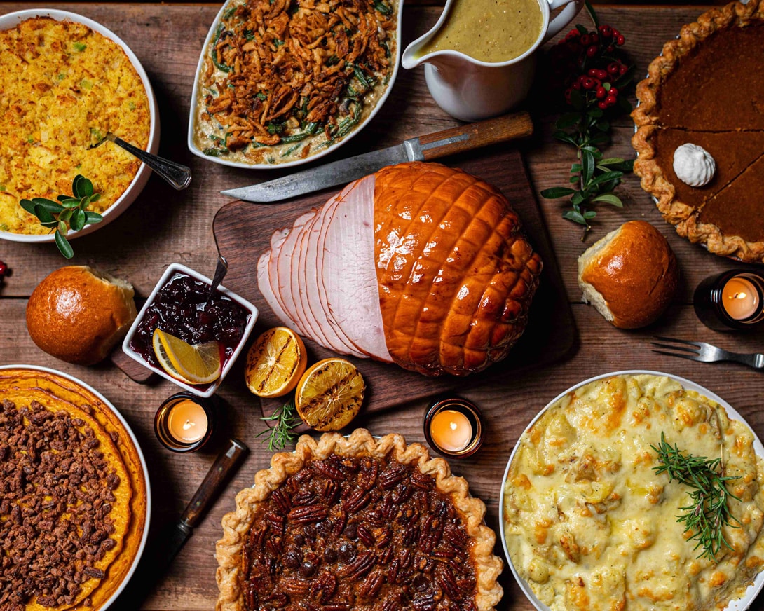 A traditional thanksgiving feast with pies, mashed potatoes, dressing/stuffing, gravy, and a large turkey in the middle.