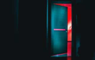 Door slightly ajar in dark room with ominous red glow emanating from the other side