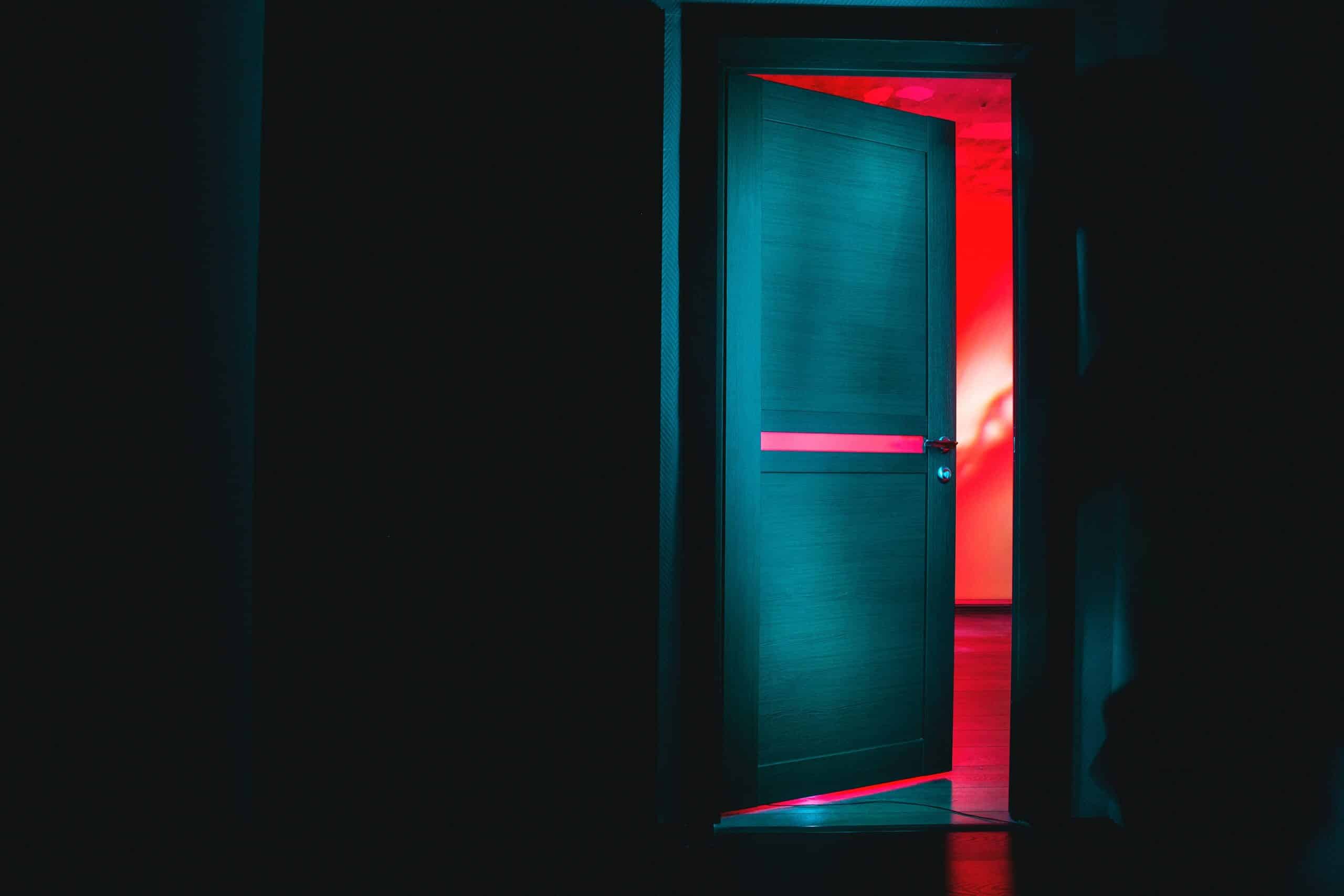 Door slightly ajar in dark room with ominous red glow emanating from the other side