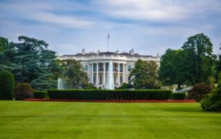 Rear view of the White House with lawn and garden in the foreground and blue sky in the background.