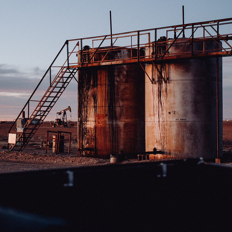 Rusted Oil Drums with a Pumpjack in the back.