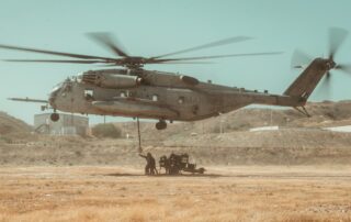 Marines loading ordinance under a hovering helicopter in an open field at a Marine Base