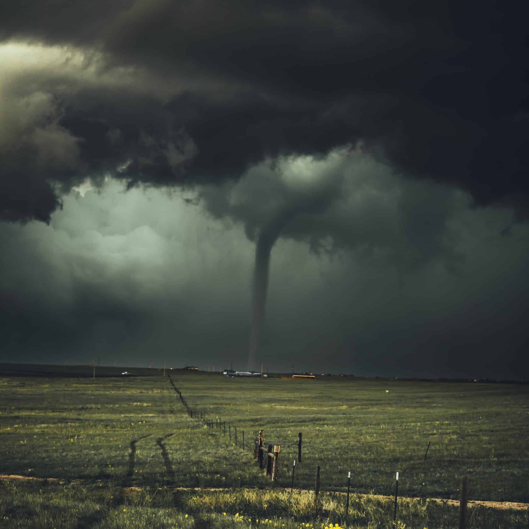 Dark and moody picture of a massive stormy sky over a small Wyoming homestead with a wide field in the foreground. All connected my a tornado spout