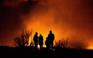 A raging wildfire at night with a family in the foreground watching.
