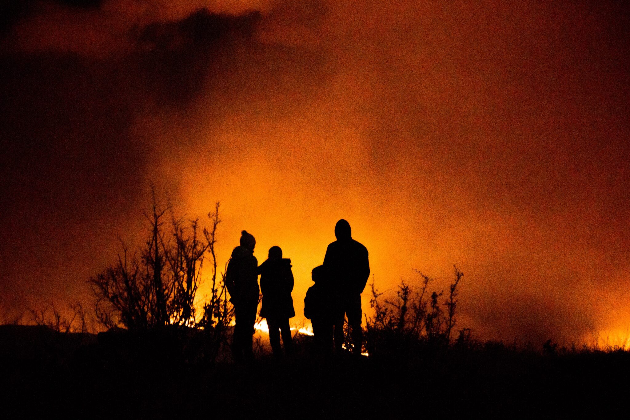 A raging wildfire at night with a family in the foreground watching.