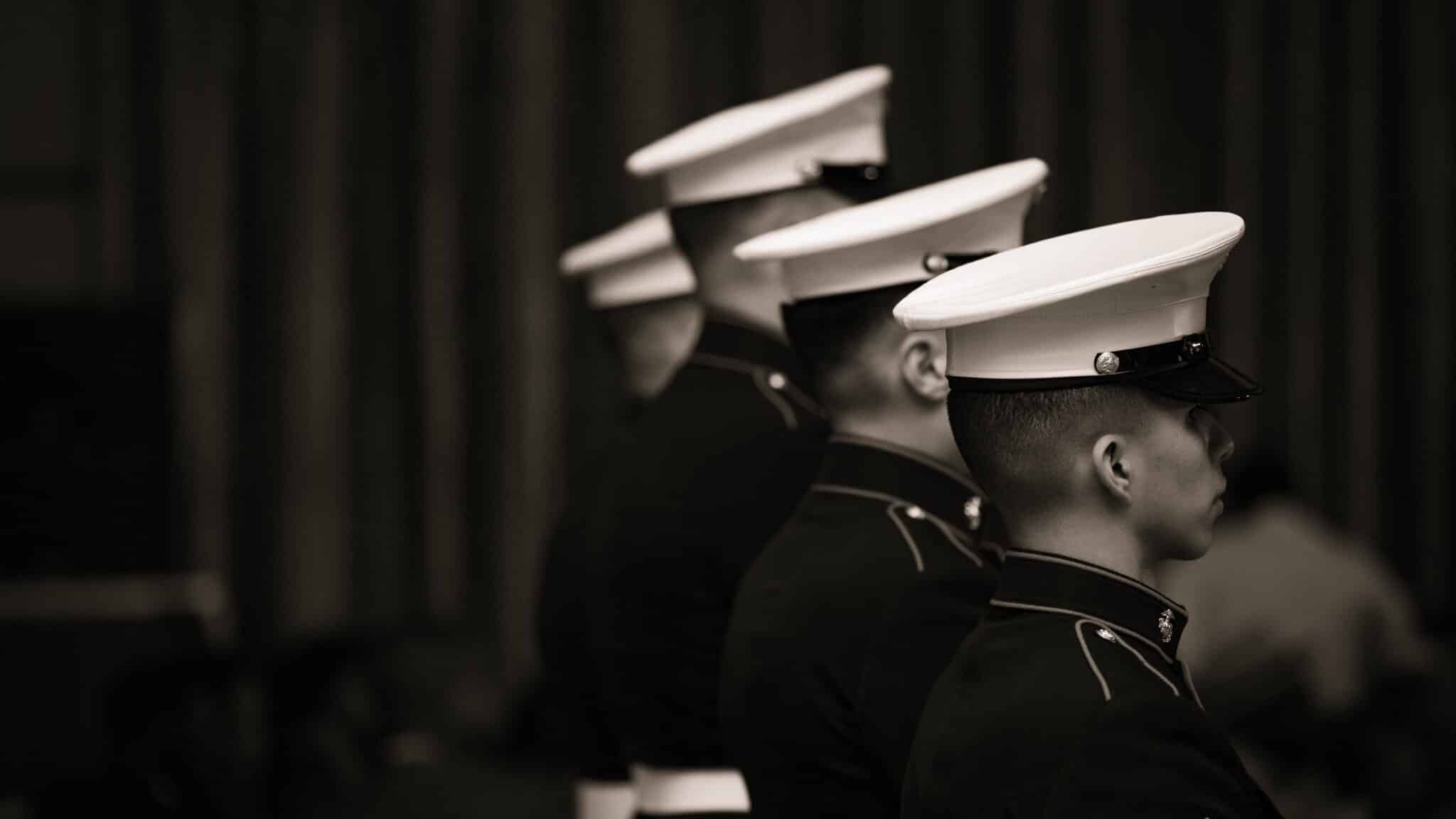 A sepia tone image of four U.S. Marines in "Dress Blues" standing in a line