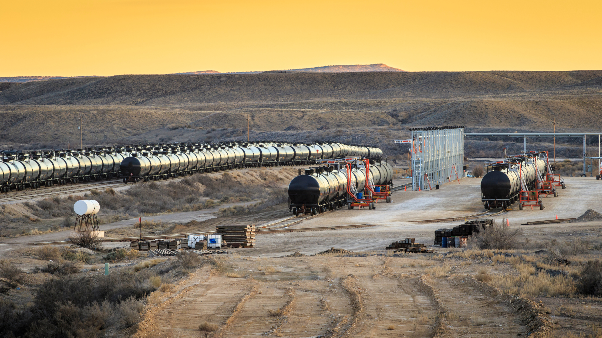 Oil tankers in Utah at a cargo railway depot with a yellow sunset sky in the foreground.