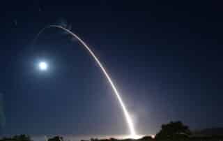 A Minuteman III ICBM missile launches at night with a bright white streak trailing it.