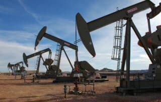 A row of oil pumpjacks with a cloudy blue sky in the background