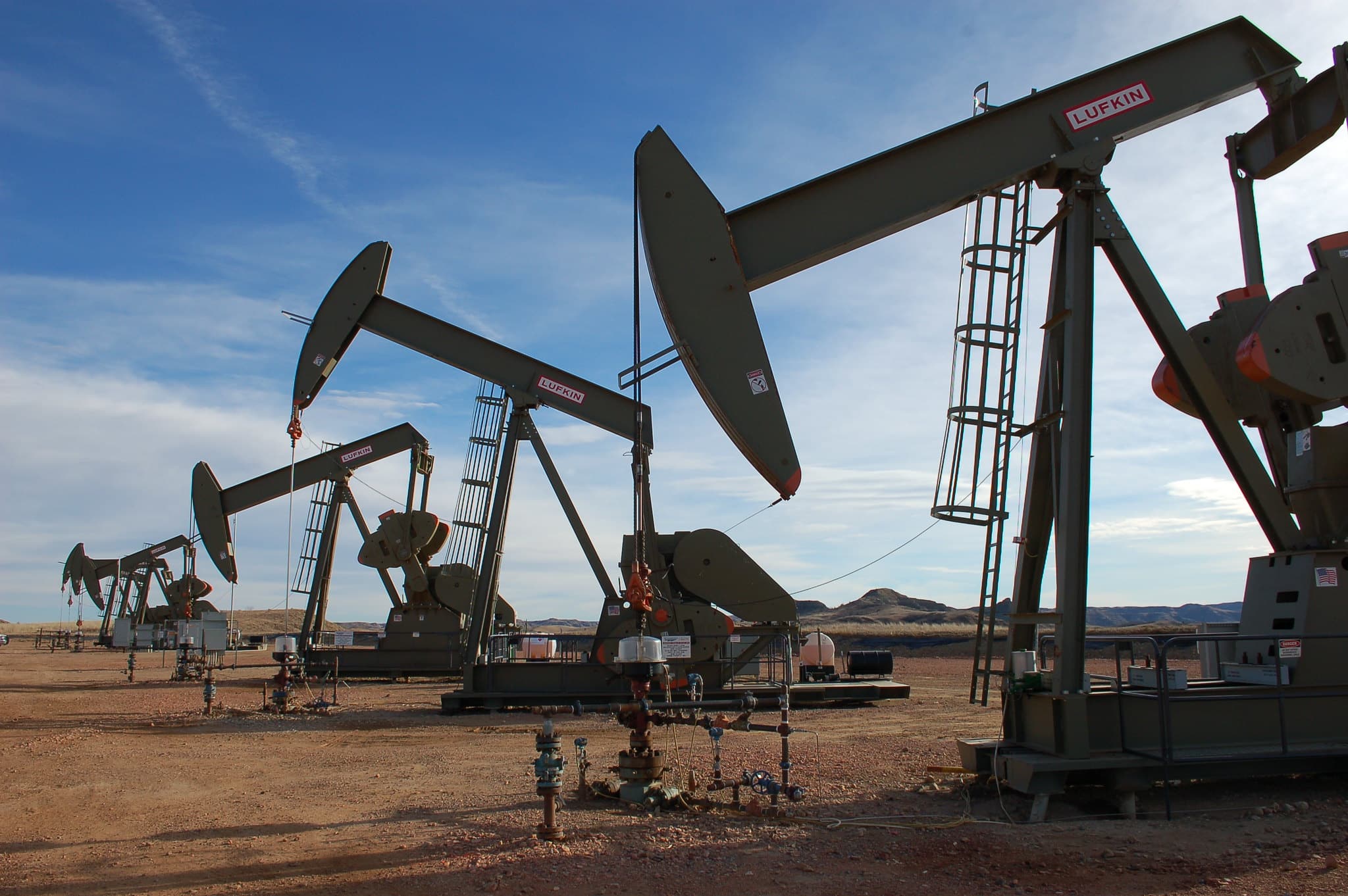 A row of oil pumpjacks with a cloudy blue sky in the background