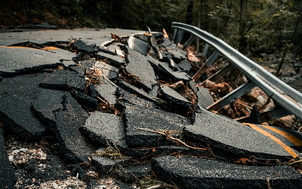 Rubble from a collapsed road with a twisted guardrail in the background