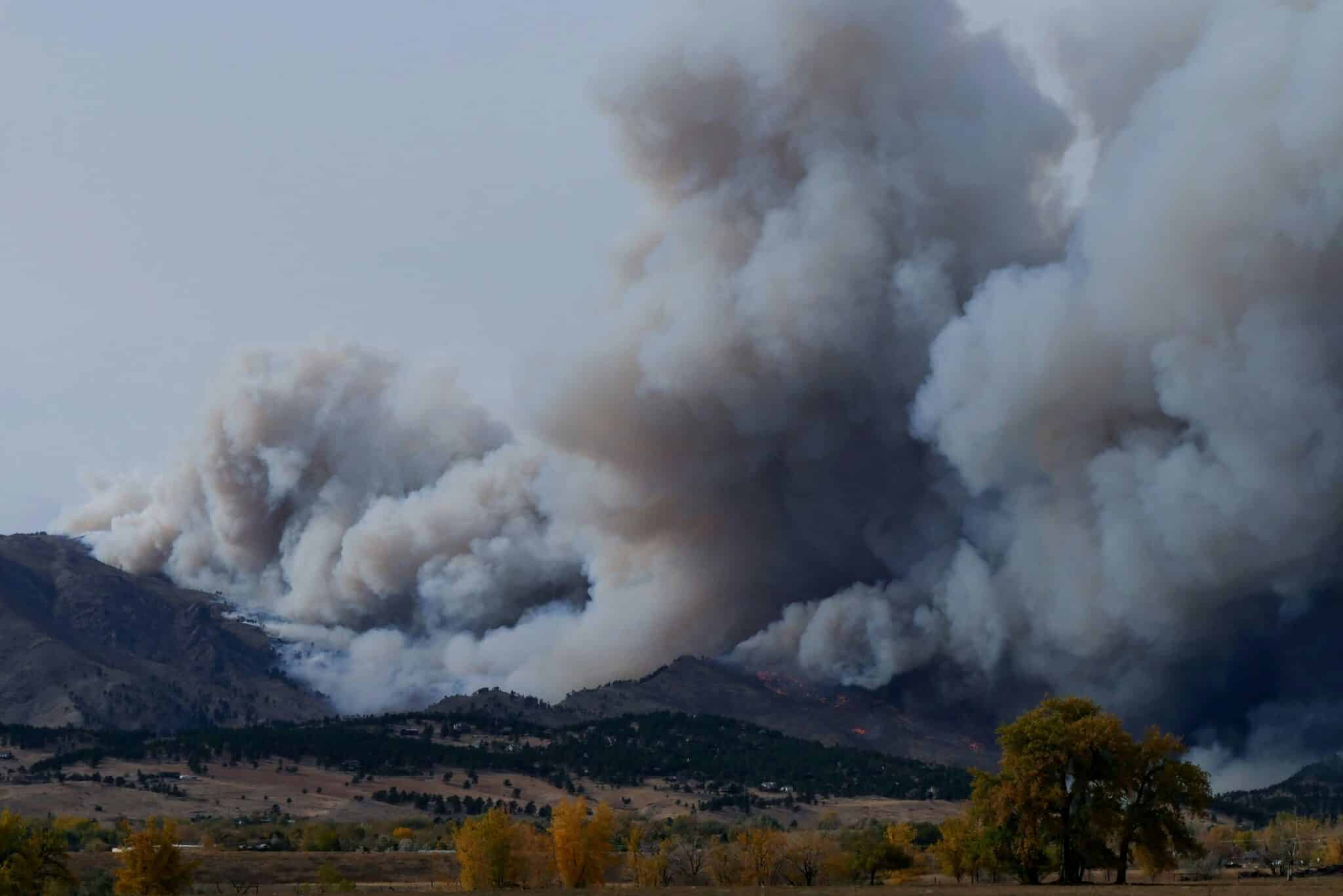 Large plume of grey smoke billows from a mountain wildfire