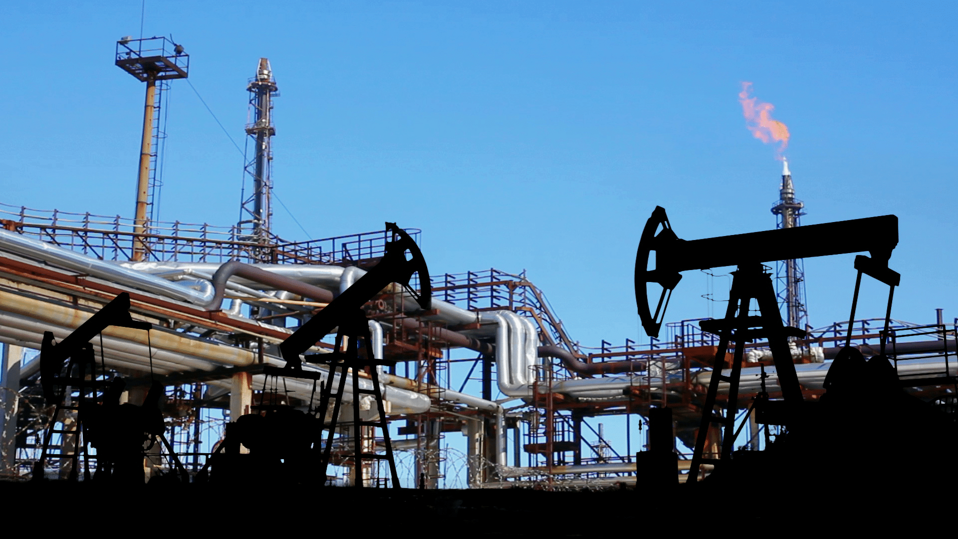 oil refinery expelling methane in the background with oil pumpjacks at work in the foreground.