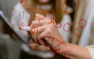 Woman with red marker writes calculations on glass surface