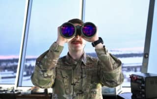 A soldier looks through large binoculars.