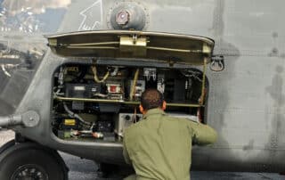 Man dressed in green coveralls works on a large military helicopter