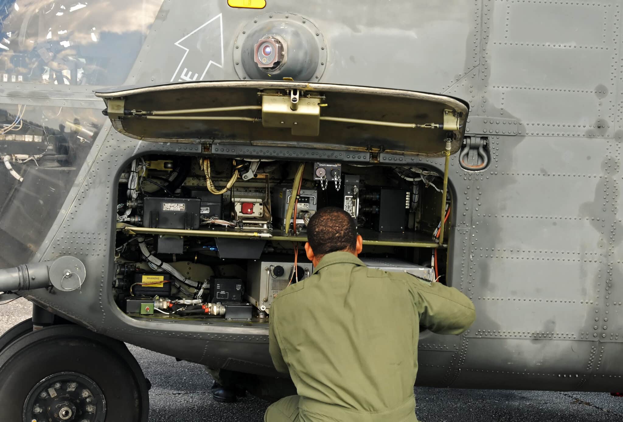 Man dressed in green coveralls works on a large military helicopter