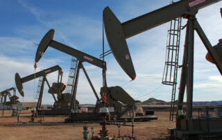 A row of oil pumpjacks with a cloudy blue sky in the background