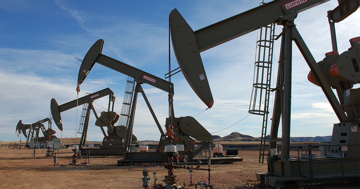 A row of oil pumpjacks with a cloudy blue sky in the background