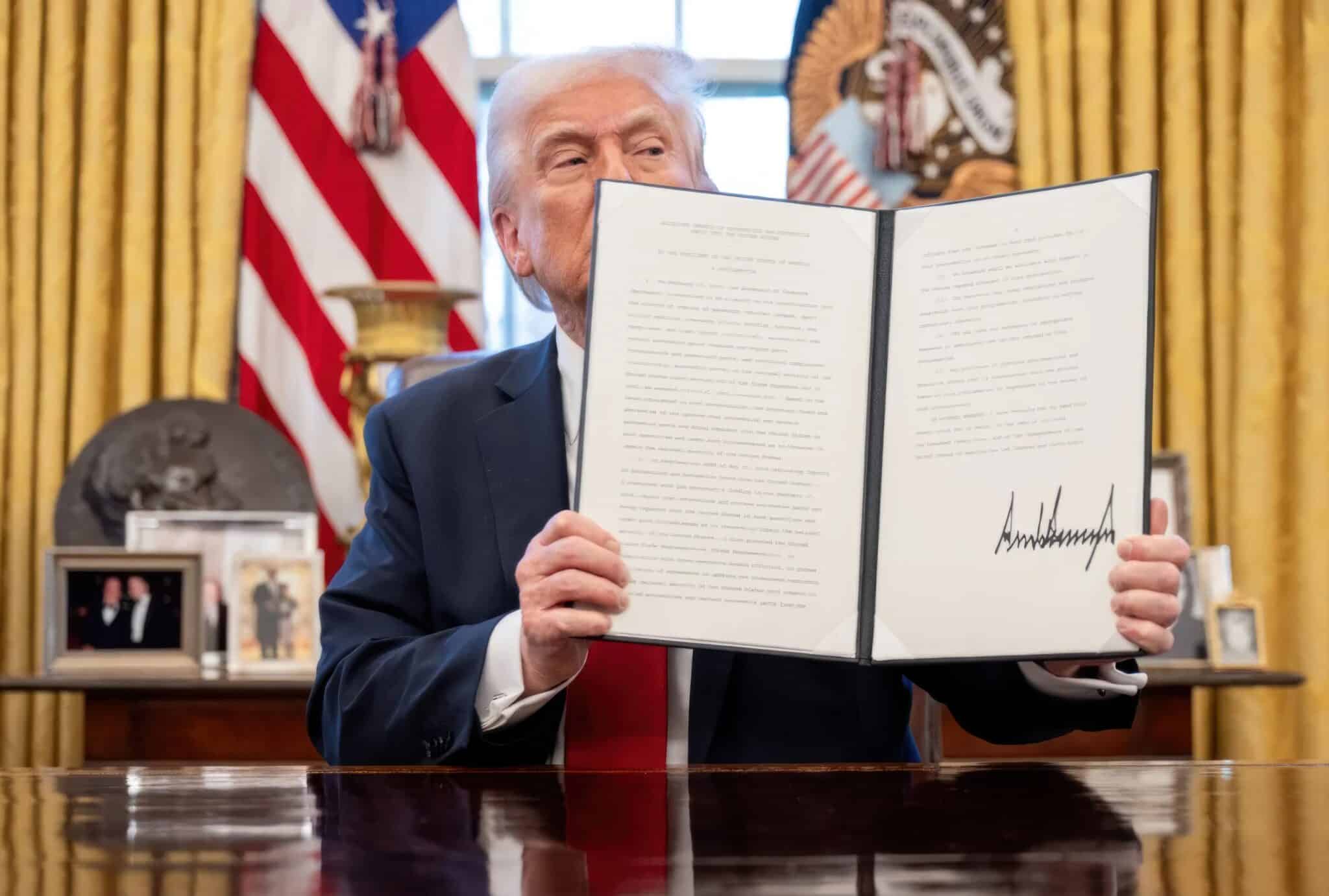 President Trump holds up a signed document in the oval office
