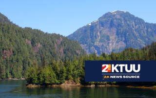 a breathtaking view of Misty Fjords with a big river in the foreground and wooded mountains in the back.