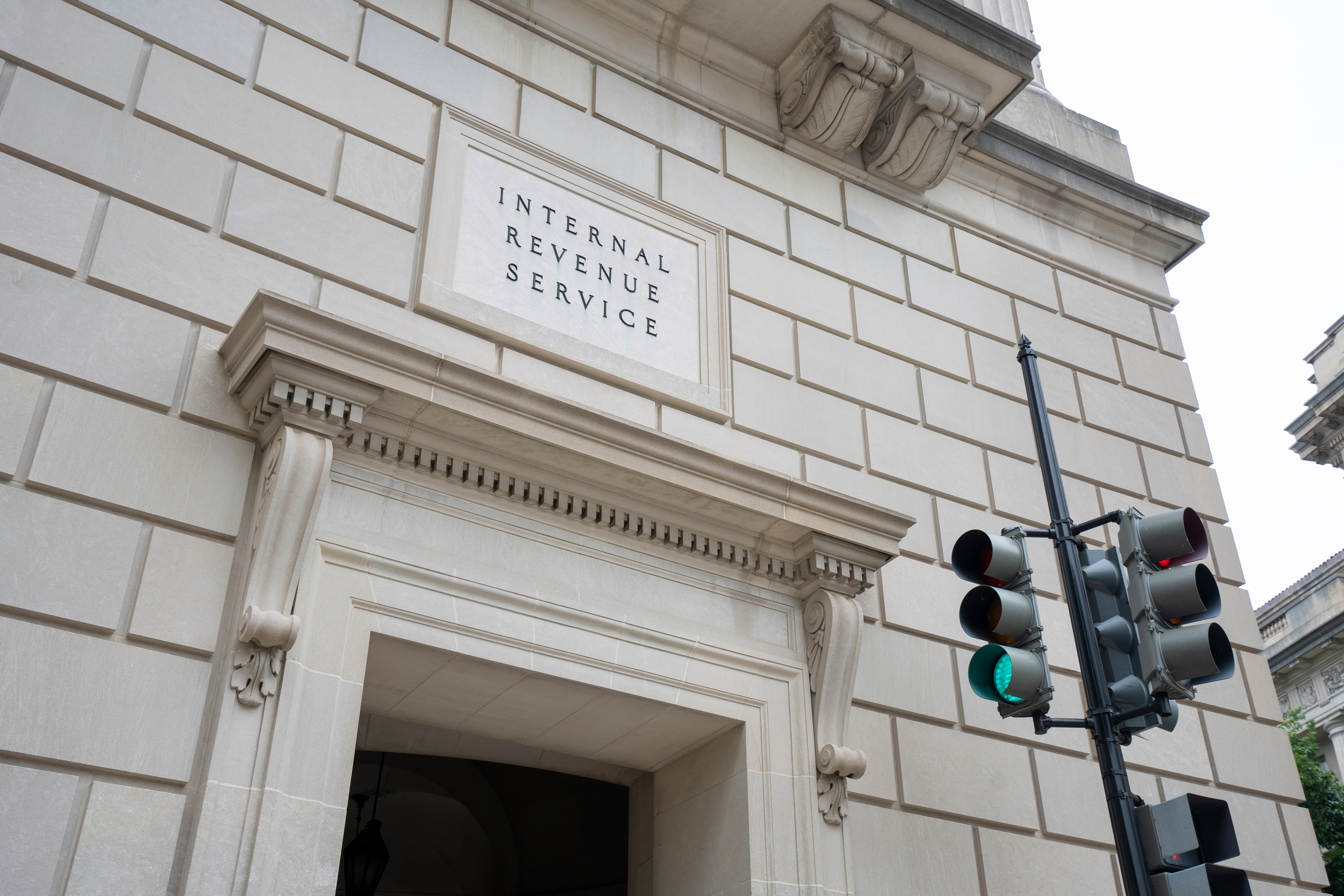 he Internal Revenue Service (IRS) Building, located in the center of the Federal Triangle complex in Washington, DC with a stoplight emerging from the bottom-right lower third of the image.